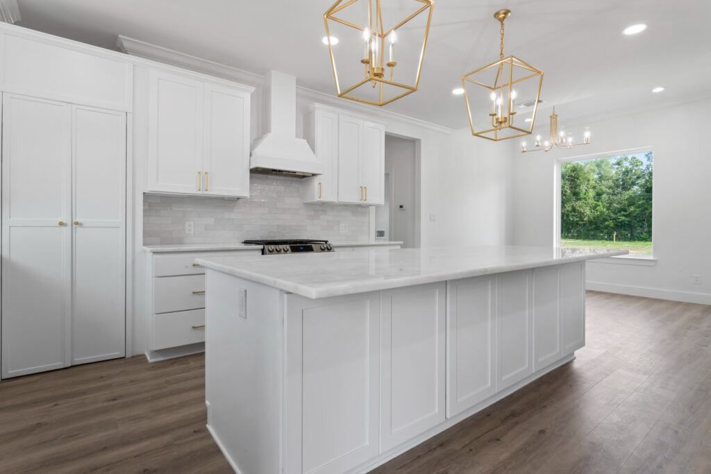 White kitchen with island, gold chandeliers, and a window overlooking greenery.