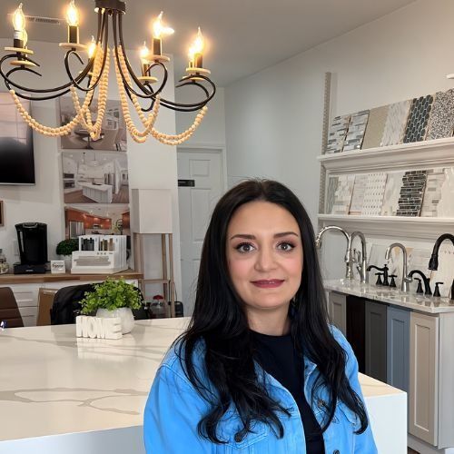 Woman in blue denim jacket in kitchen showroom, smiling, looking at camera.