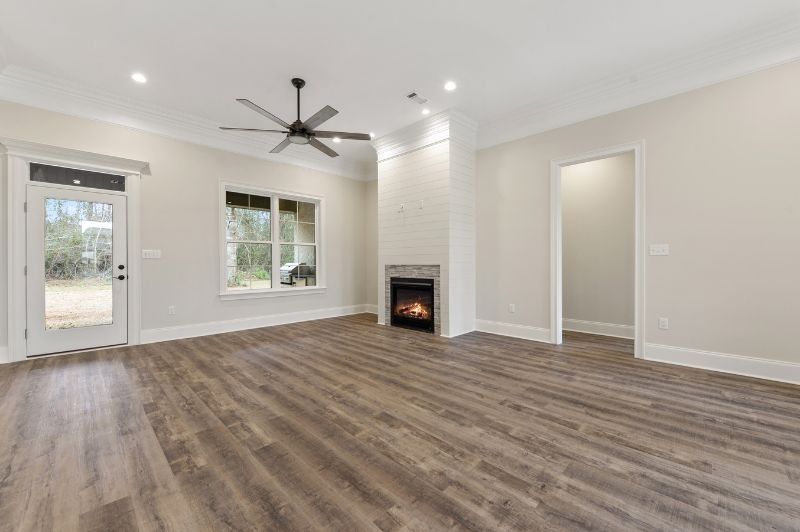 Empty living room with fireplace, hardwood floors, ceiling fan, and window.