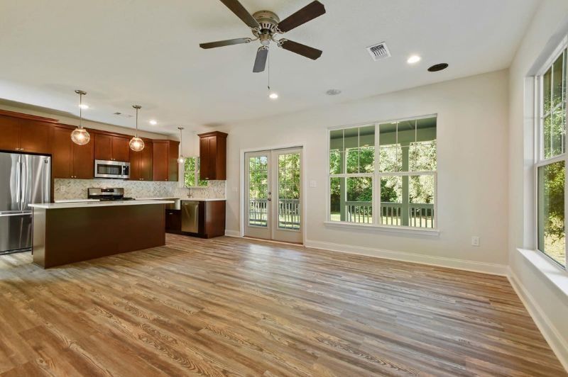 Open-concept kitchen and living area with wood floors, dark cabinets, and French doors leading to a covered porch.