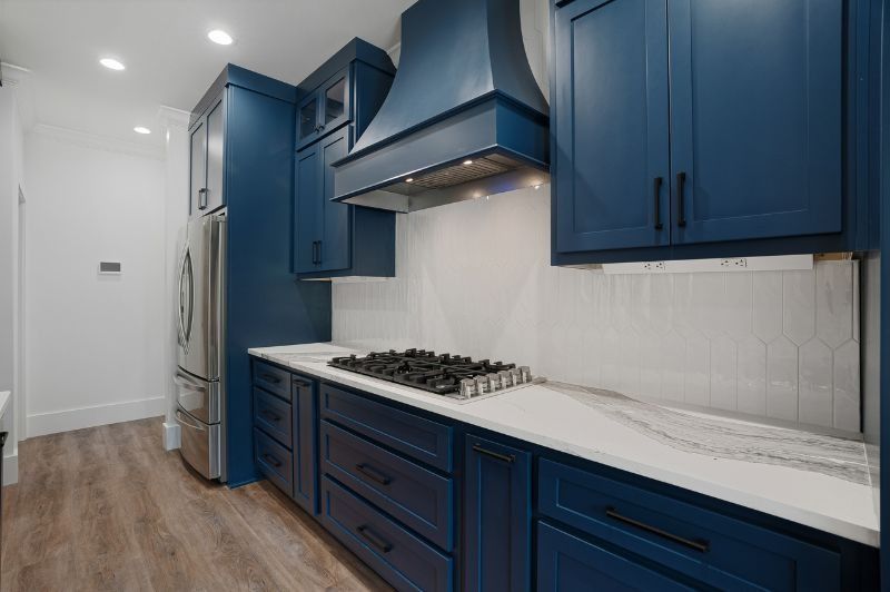 Blue kitchen with white countertops, gas stovetop, and stainless steel appliances.