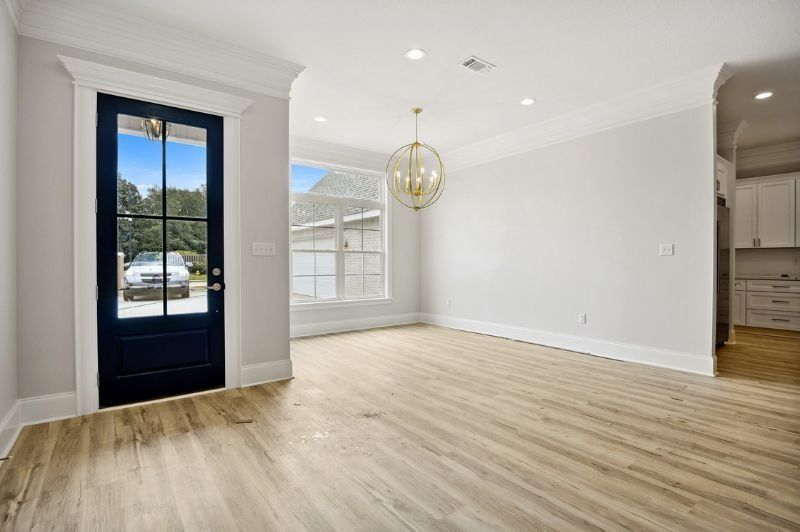 Empty dining room with wood floor, a black front door, and gold chandelier.