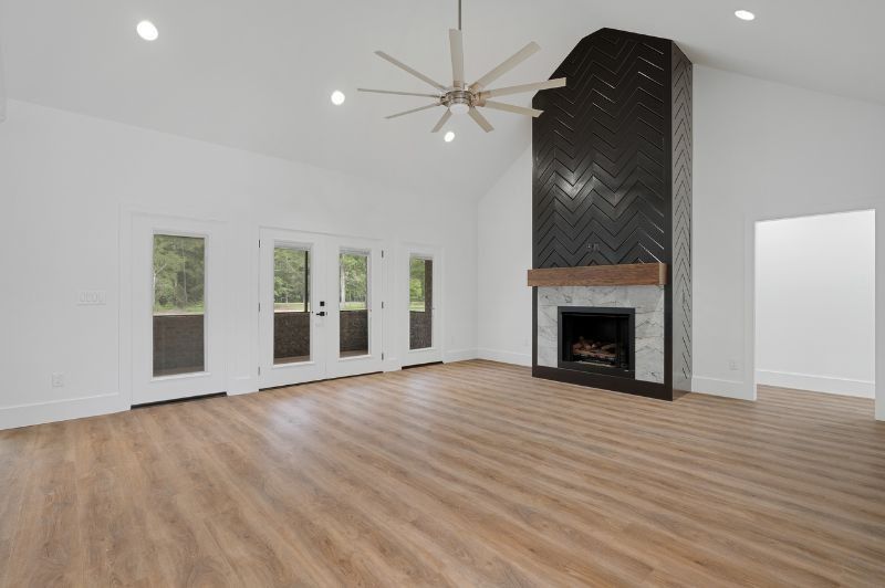 Spacious white living room with black tiled fireplace, wooden mantel, and light wood floors.