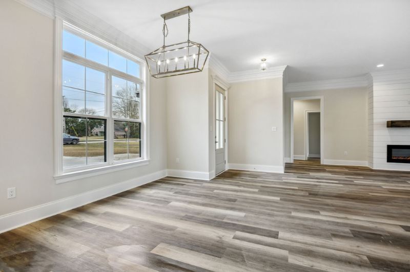 Empty dining room with large window, gray wood floor, and modern chandelier.