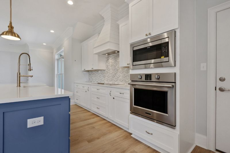 A bright, modern kitchen with white cabinets, stainless steel appliances, and a blue island.