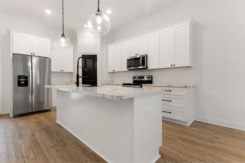 Modern white kitchen with stainless steel appliances, white cabinets, and a kitchen island with granite countertop.