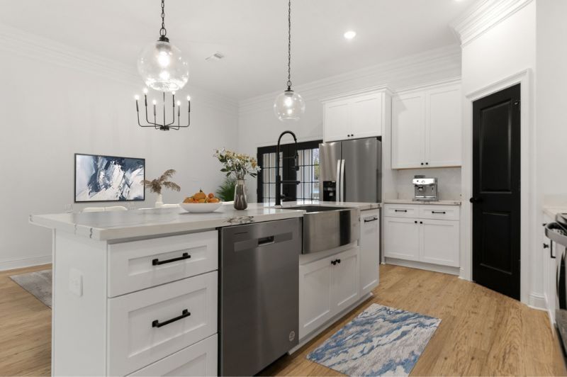 Modern kitchen with white cabinets, stainless steel appliances, island, and black accents.