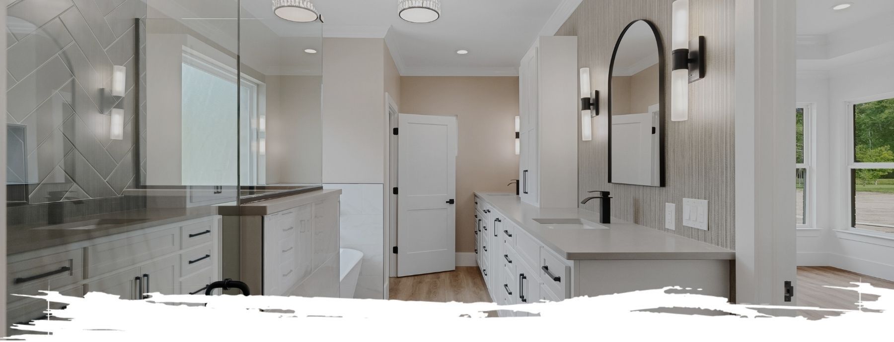 A bathroom with white cabinets, light gray countertops, a black arched mirror, and a glass shower door.