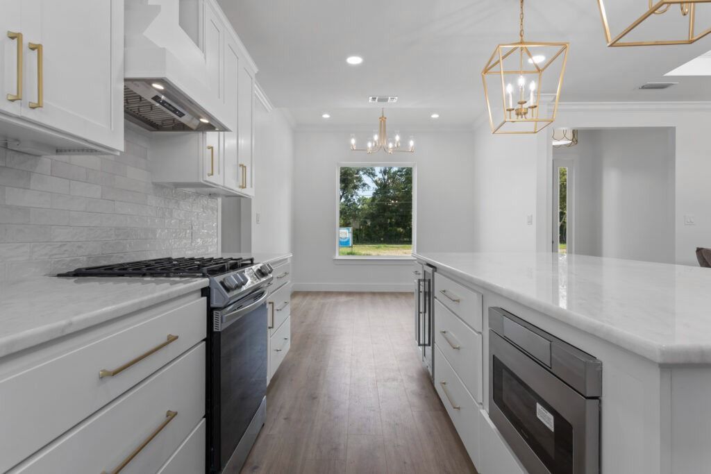 Modern white kitchen with gold hardware and a large island, with a view to the outdoors.