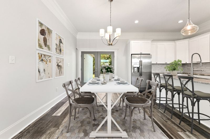 Dining room with white table, chairs, artwork, chandelier, and open to a kitchen with bar stools.