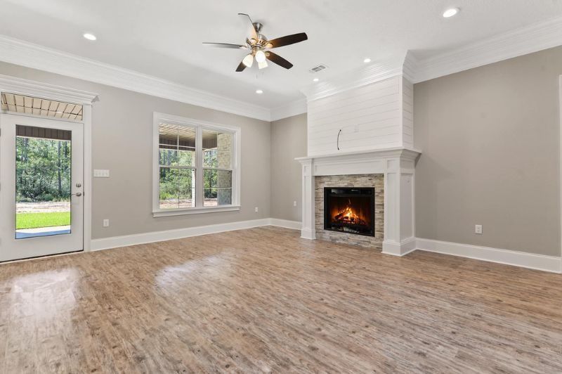 Empty living room with fireplace, wood floor, and a door to a backyard.