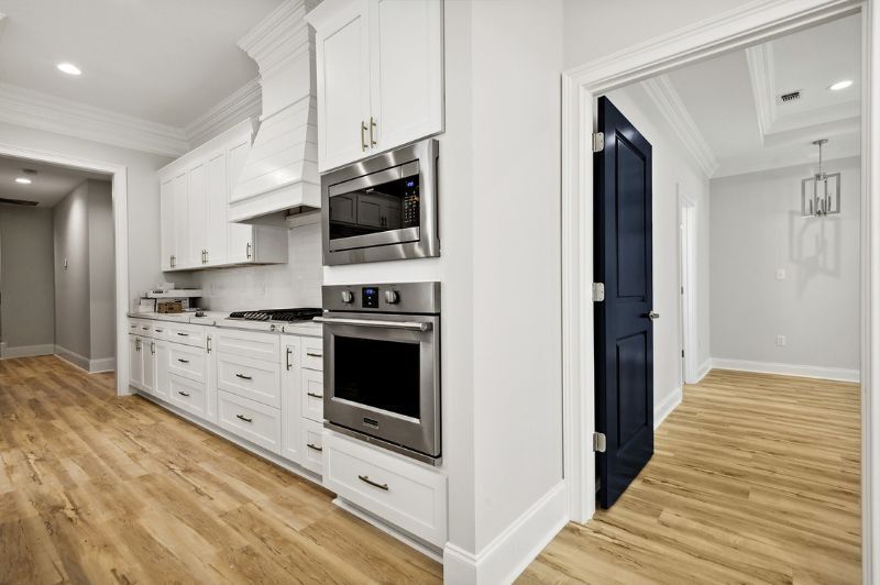 White kitchen with stainless steel appliances, light wood floors, and an open navy blue door to another room.