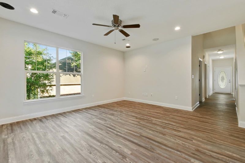 Empty room with wood-look floor, a window, ceiling fan, recessed lights, and hallway with a door.