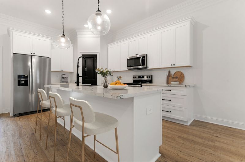 Modern white kitchen with island seating, stainless steel appliances, and light wood floors.