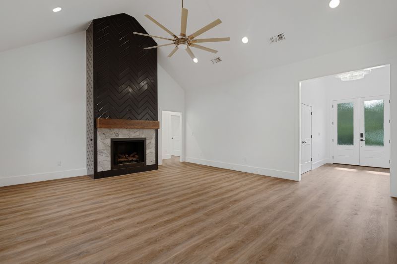 Empty, bright living room with fireplace, high ceiling, wooden floor, and a double-door entrance.