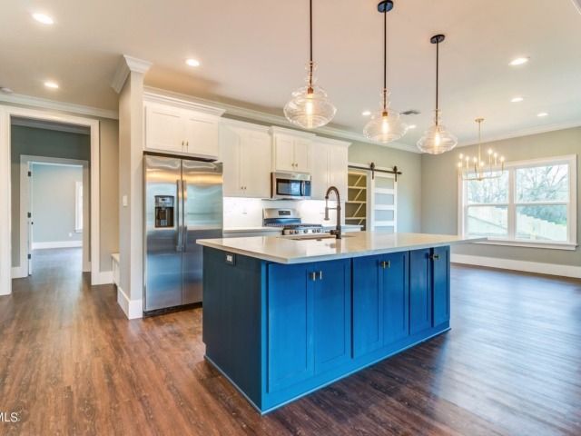 Blue kitchen island with white countertops, stainless steel appliances, and wooden floors.