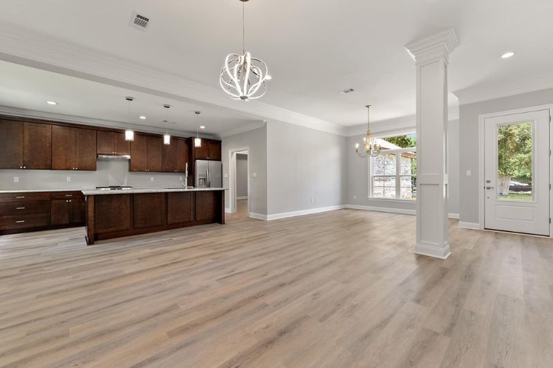 Open-concept kitchen and living area with dark brown cabinets, gray walls, and light wood flooring.