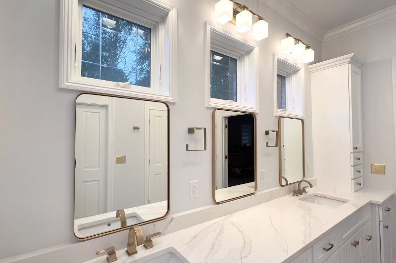 Bathroom with white cabinets, marble countertop, gold mirrors, and vanity lights.