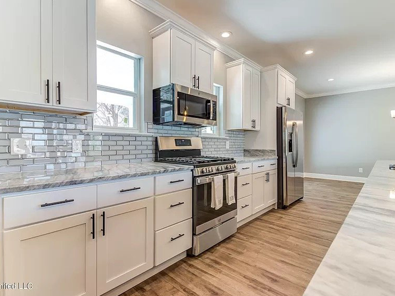 White kitchen with stainless steel appliances, white cabinets, and light granite countertops.