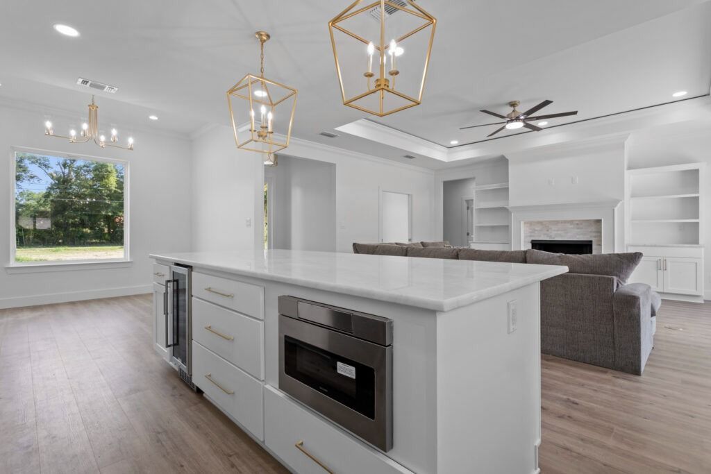 Open-concept white kitchen with island, gold light fixtures, and living area with a fireplace.