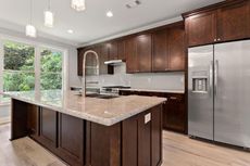 Modern kitchen with dark brown cabinets, large island, stainless steel appliances, and a bright window.