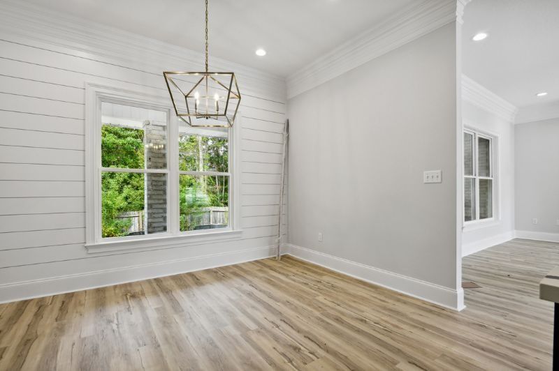 Empty dining room with light wood floors, white walls, window, and a hanging geometric chandelier.
