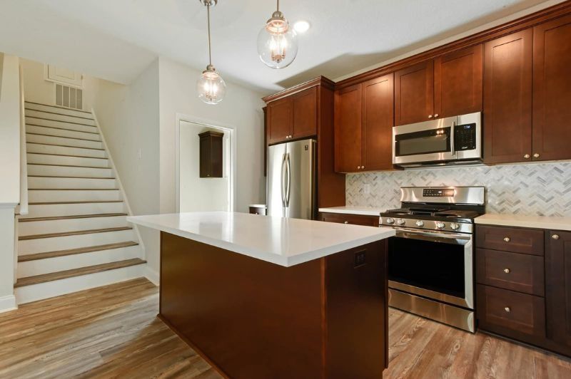 Modern kitchen with dark wood cabinets, stainless steel appliances, white island, and staircase.