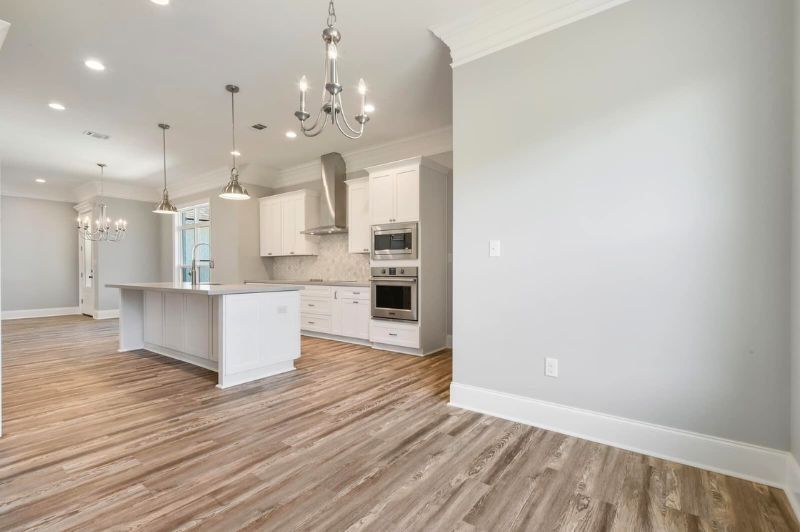 Spacious, modern kitchen with white cabinetry, island, stainless steel appliances, and wood-look flooring.