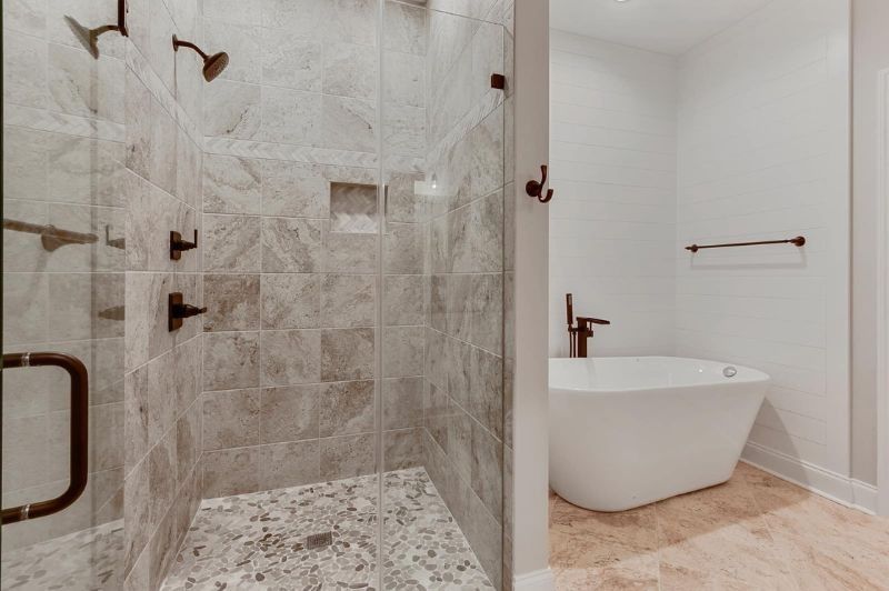 Shower with glass door, marble tiles, and a free-standing bathtub in a bright bathroom.