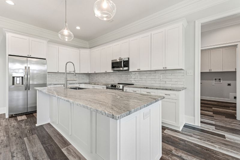 White kitchen with island, stainless steel appliances, and grey wood-look floor.