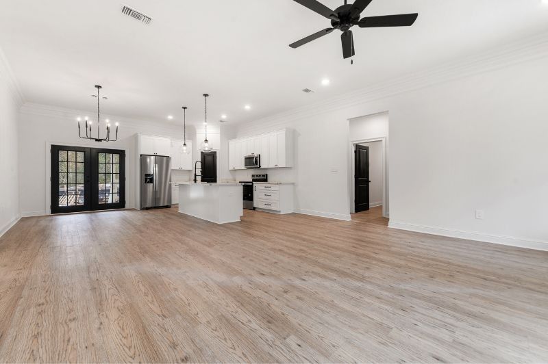 Open-concept kitchen with white cabinetry, island, and stainless steel appliances; light wood floors and black accents.