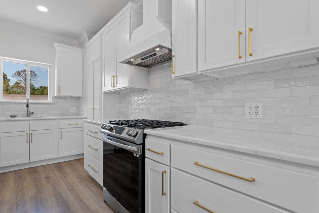 Bright white kitchen with gold hardware, stainless steel appliances, and white backsplash.