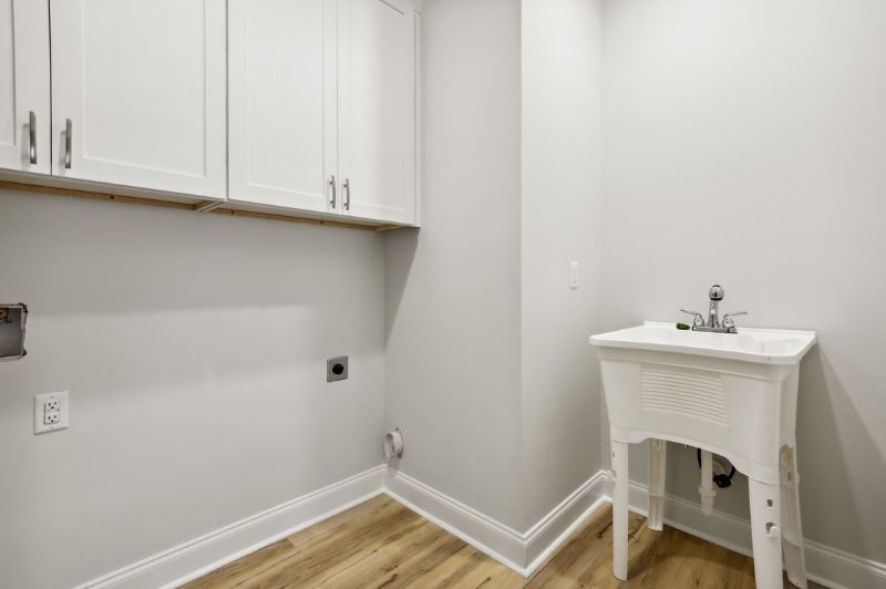 Laundry room with white cabinets, sink, and light wood-look flooring.