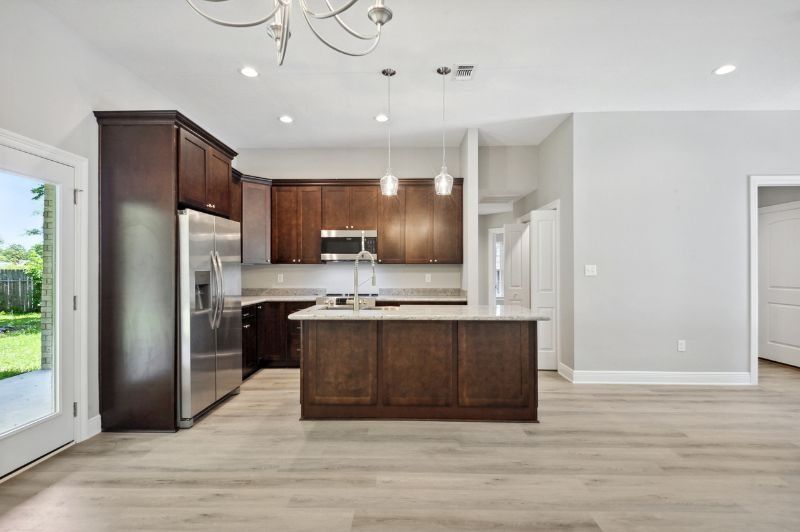 Modern kitchen with dark wood cabinets, stainless steel appliances, and a light-colored island.