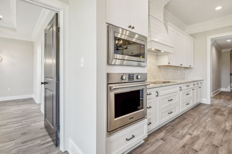 White kitchen with built-in microwave, oven, cabinets, and a doorway to a room with wood-look flooring.