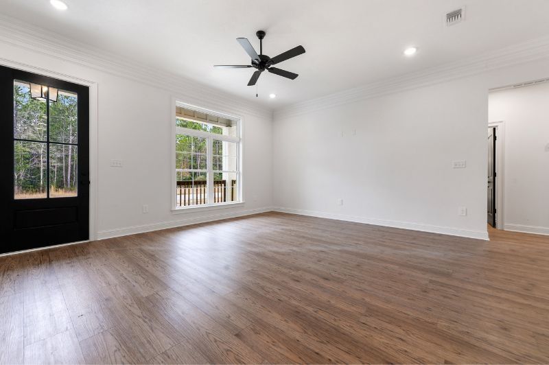 Empty room with hardwood floors, black door, large window, and ceiling fan.
