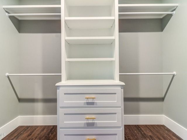 White built-in closet with shelves, drawers, and rods against a gray wall and brown floor.