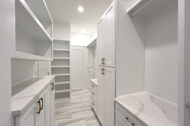White walk-in closet with shelves, cabinets, marble countertops, and gold hardware.