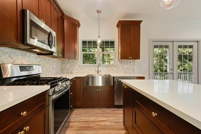 Kitchen with cherry cabinets, white countertops, stainless steel appliances, and a sink in front of windows.