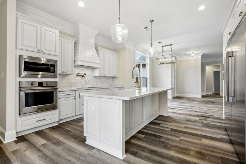 White kitchen with island, stainless steel appliances, and wood flooring.
