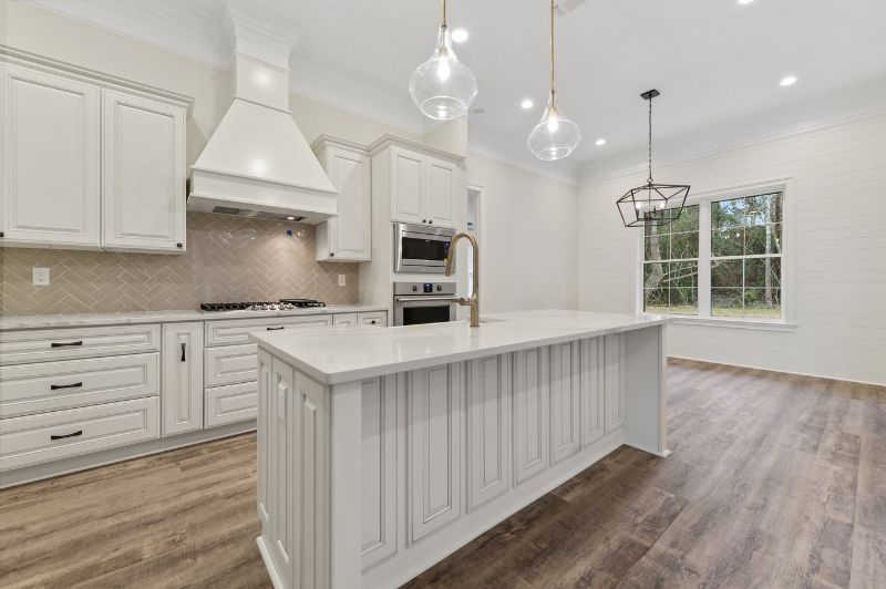 White kitchen with island, cabinets, stove, oven, and pendant lights.