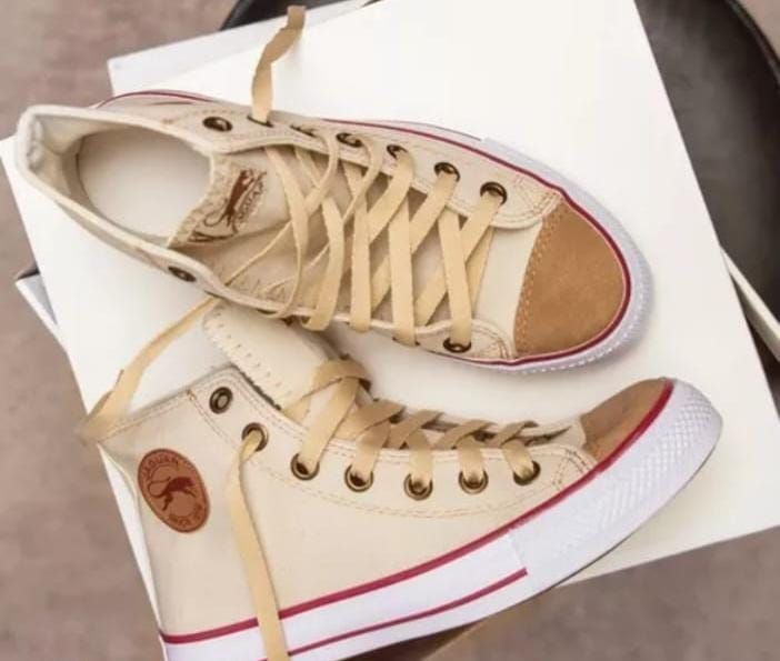 Un par de zapatillas negras de caña alta con cordones blancos en los pies de una persona.