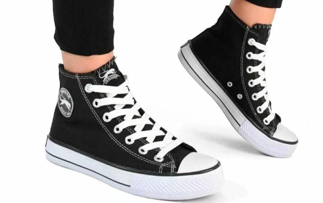Un par de zapatillas negras de caña alta con cordones blancos en los pies de una persona.