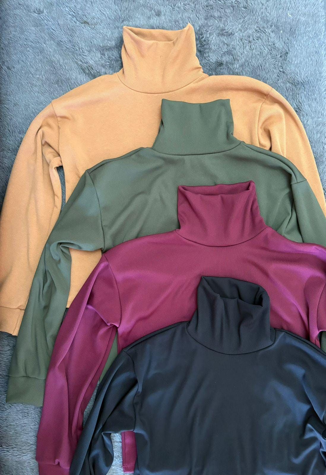 Tres suéteres de cuello alto de diferentes colores se apilan uno encima del otro.