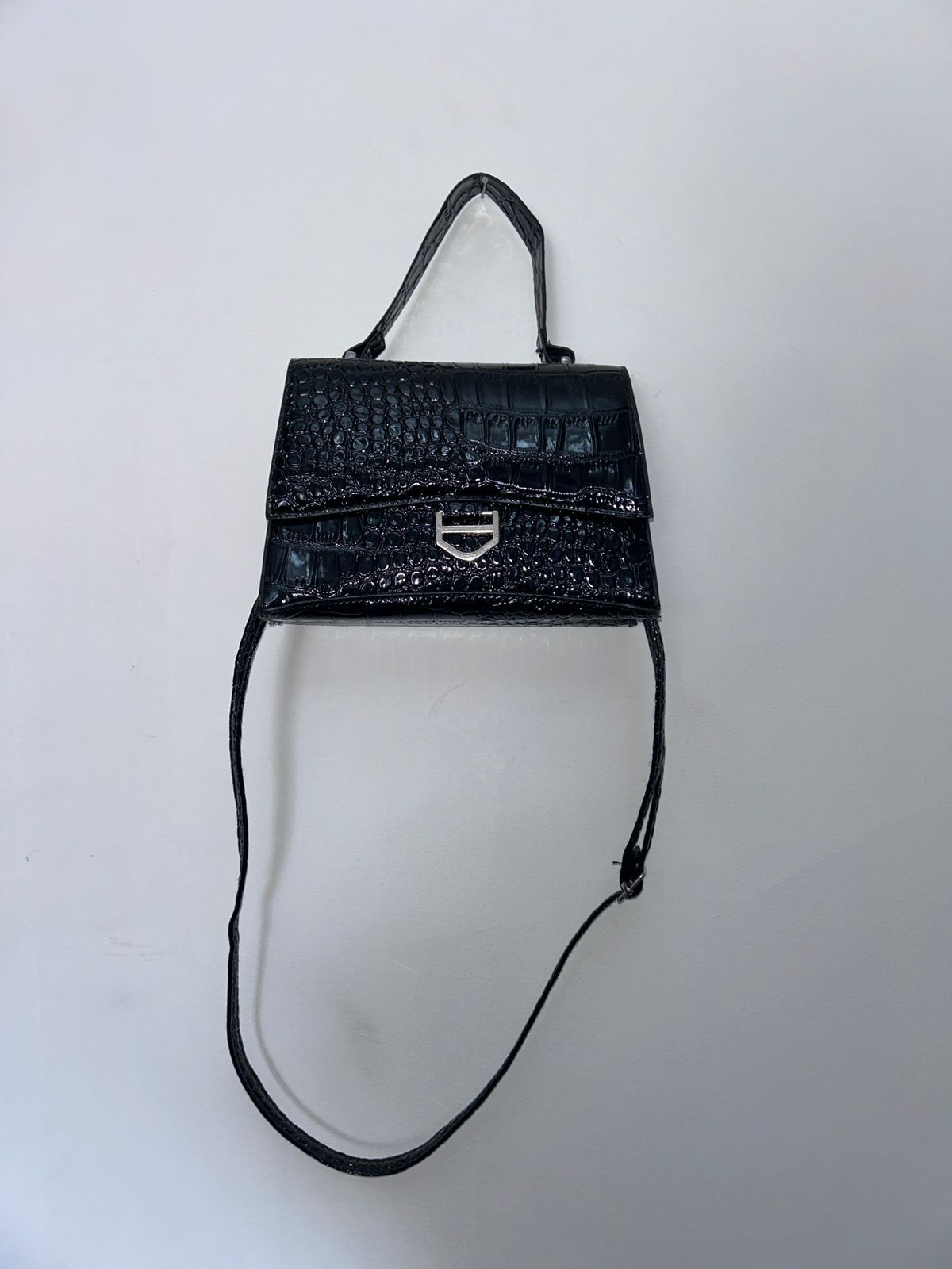 Un bolso negro con una correa larga reposa sobre una superficie blanca.