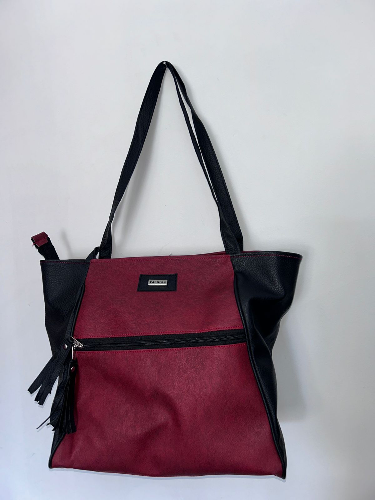 Una bolsa de mano roja y negra está colgada en una pared blanca.