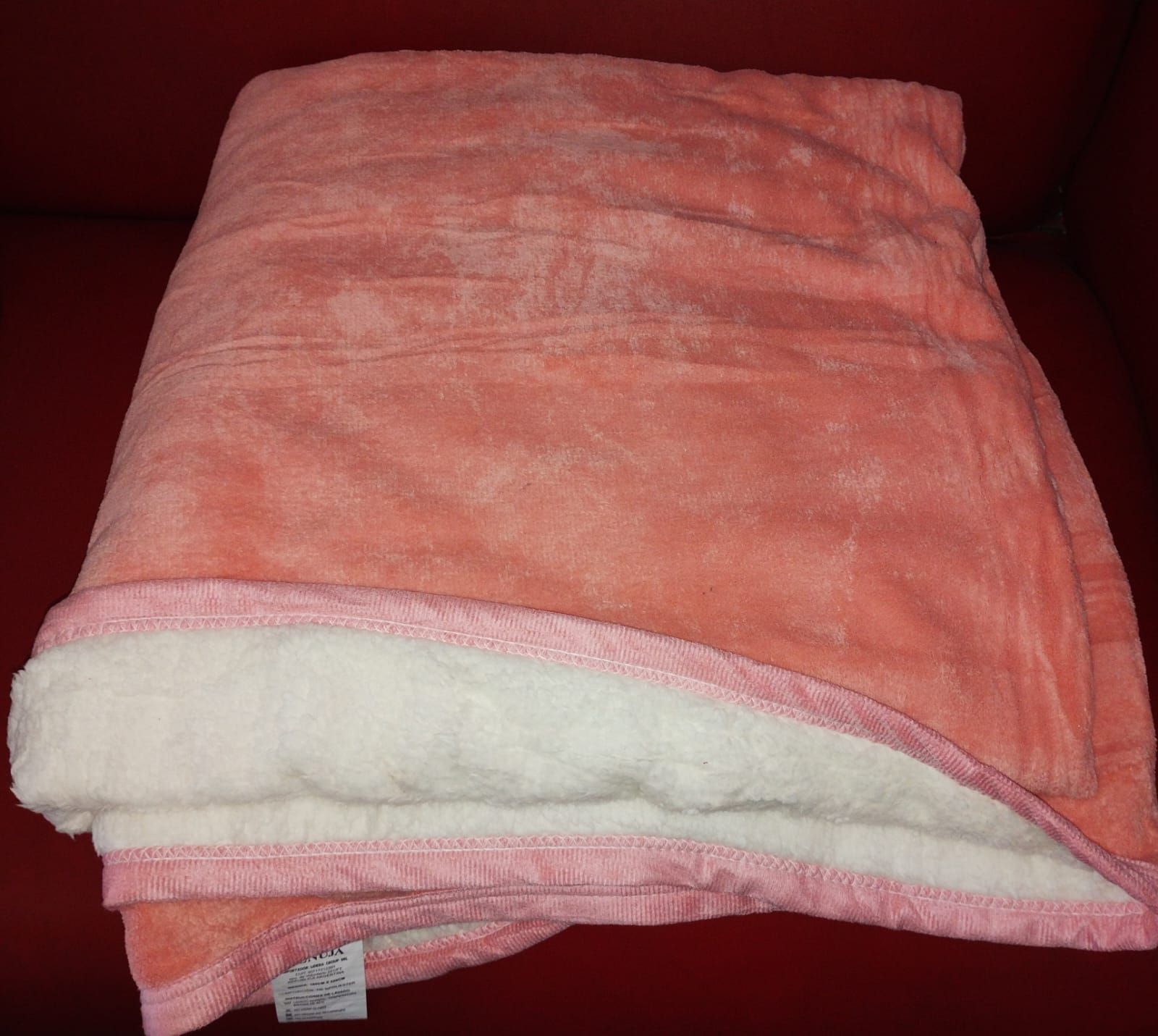 Una manta rosa y blanca está sobre un sofá rojo.