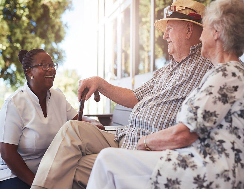 An elderly couple is sitting on a bench talking to a nurse.