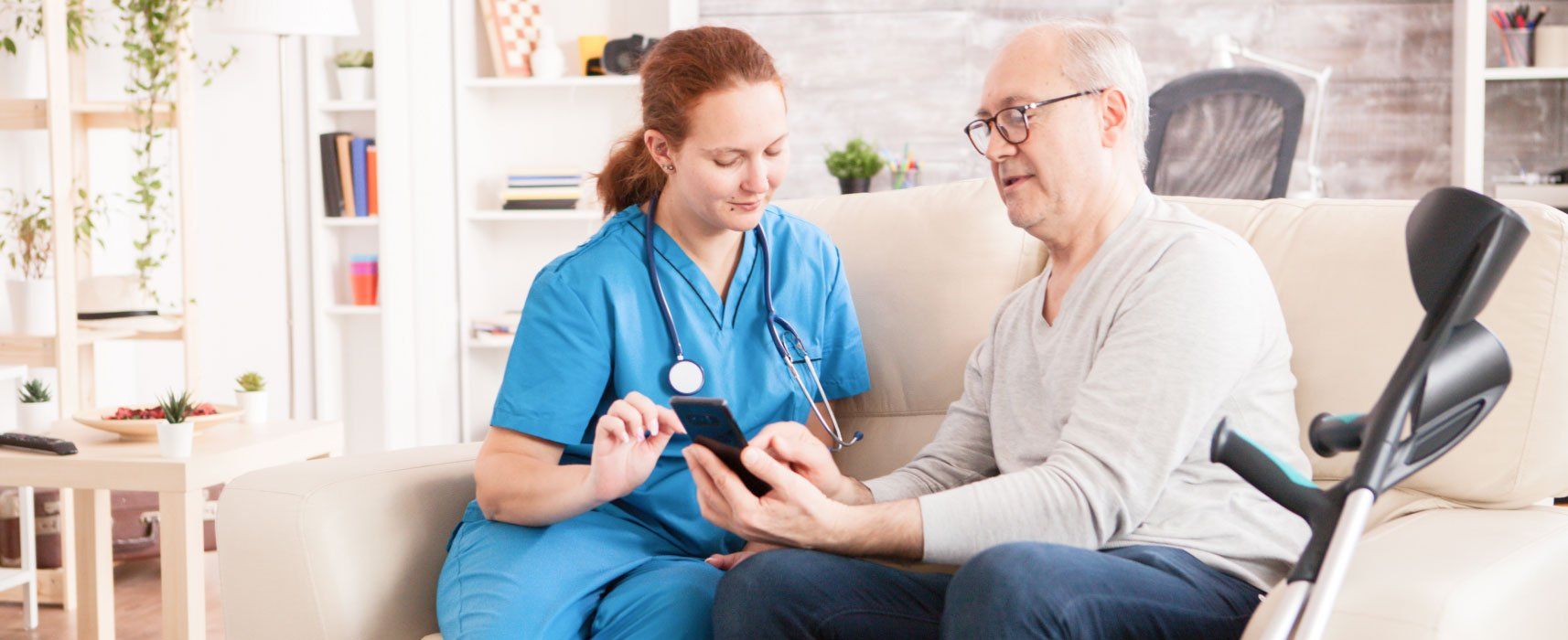 A nurse is talking to an elderly man with crutches on a couch.