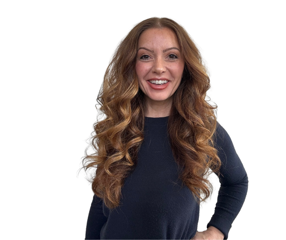 Woman with long wavy auburn hair smiles, wearing a navy blue sweater. White background.